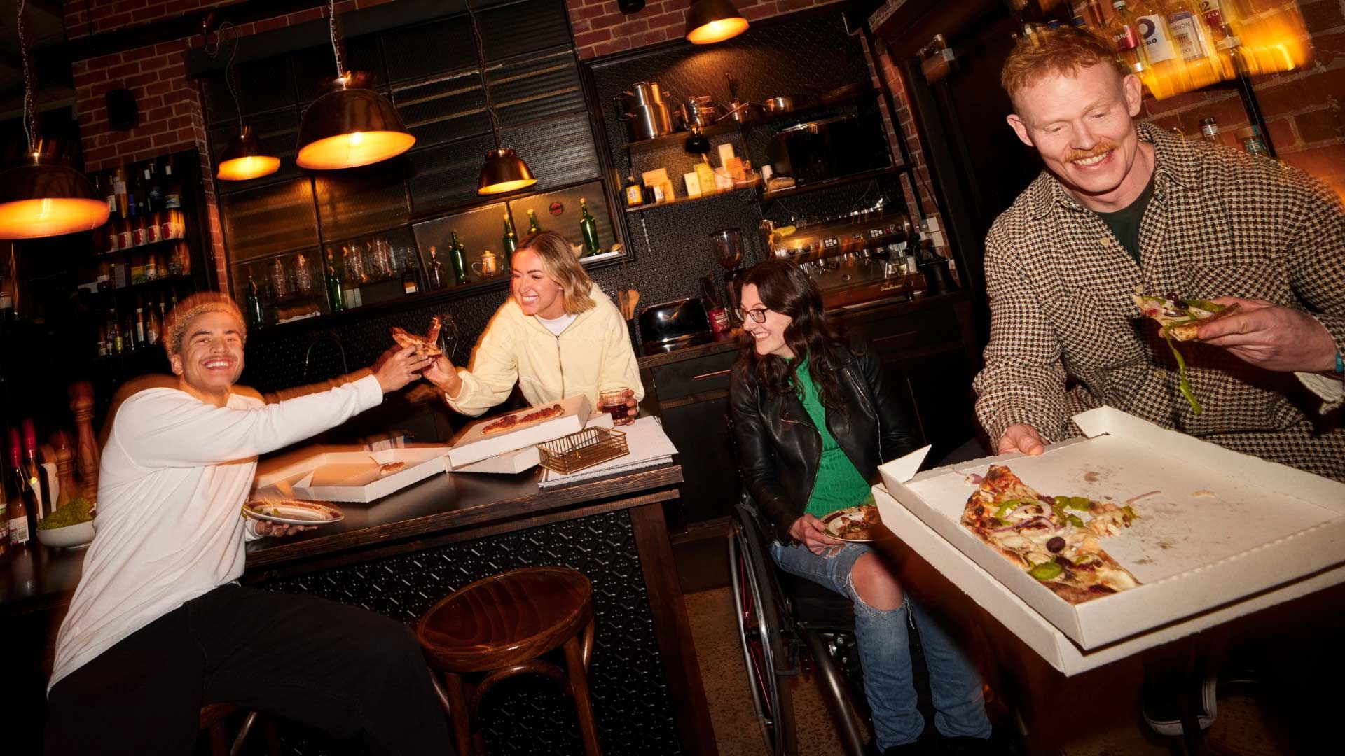 Photo of smiling people eating pizza at a bar.