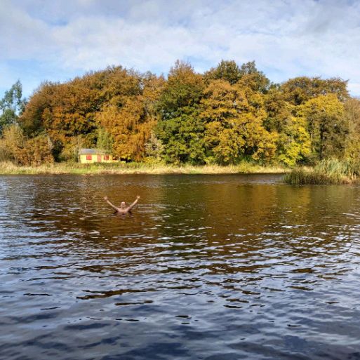 Wide shot of a lake or river. A man can be seen, half-submerged in the water.